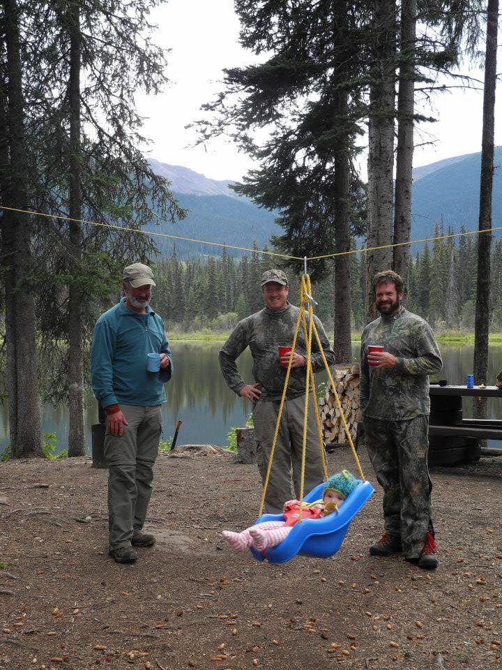 baby camping with swing attached to line three men in the background