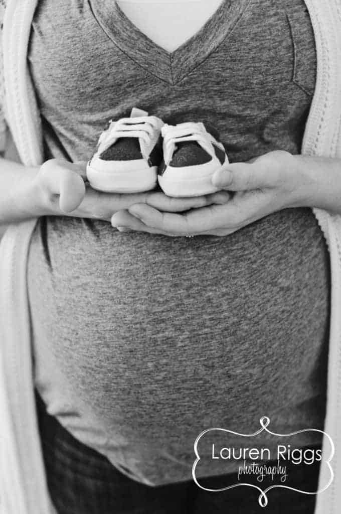 black and white photo of pregnant woman holding baby shoes