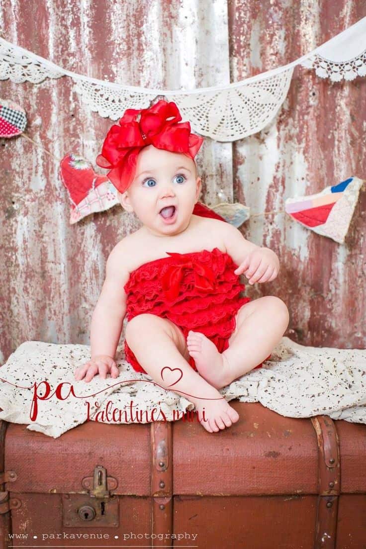 Baby making surprised face wearing red outfit with giant red bow