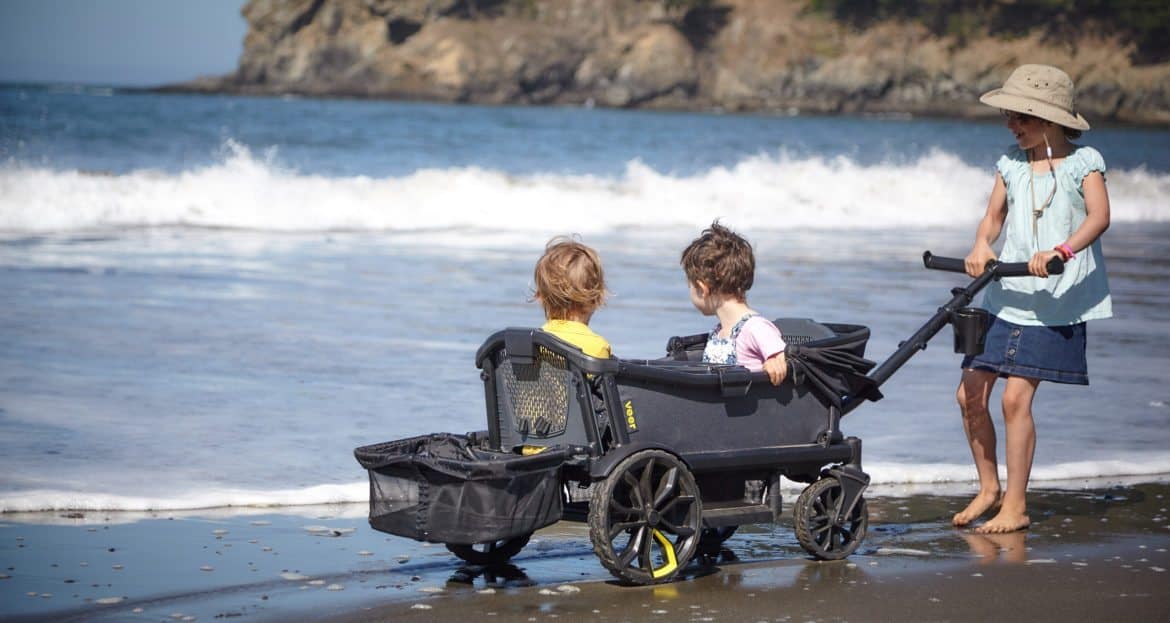 two kids sitting in a Veer stroller wagon while girl pulls it on the beach