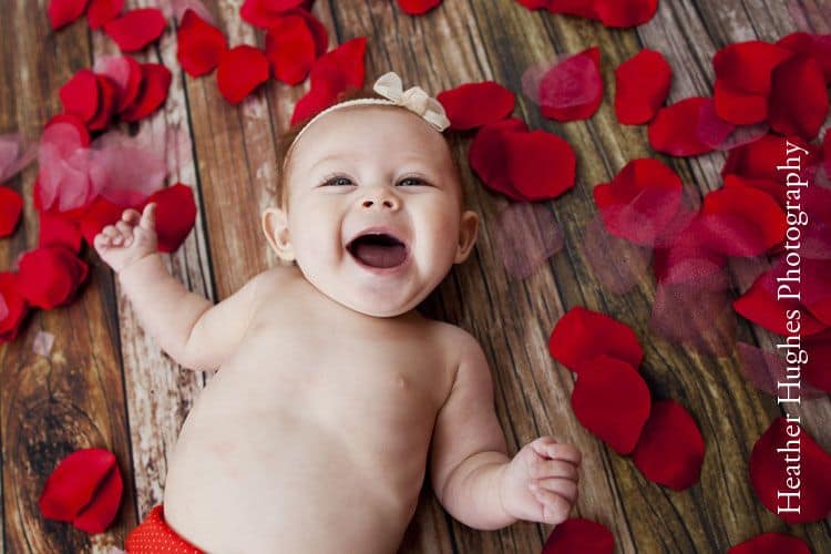 Laughing baby laying on floor surrounded by rose petals