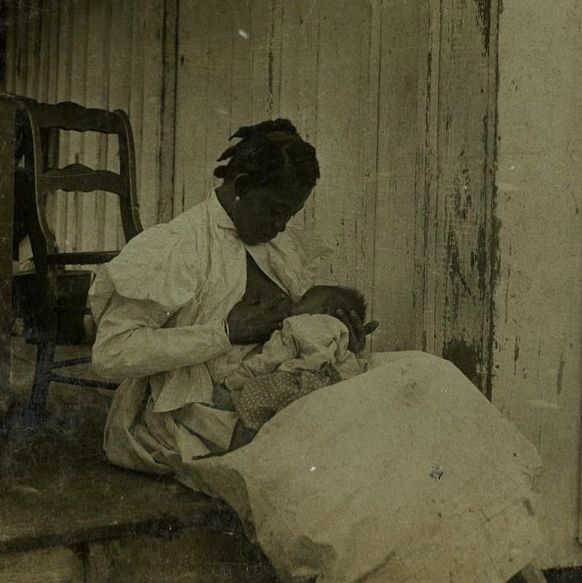 Black and white photograph of dark haired mother smiling down at nursing baby
