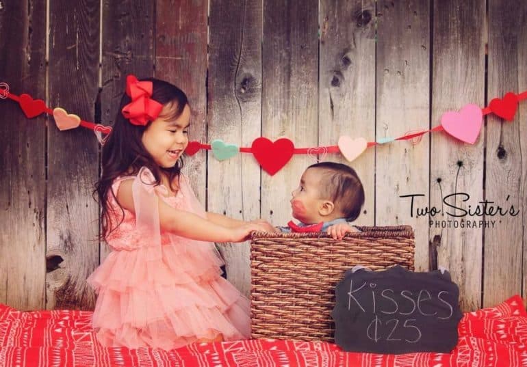 siblings sitting next to each other in homemade kissing booth Baby's First Valentine's Day Photo shoot