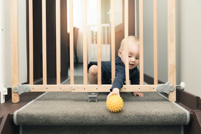 baby trying to grab yellow ball through safety gate at the top of the stairs.