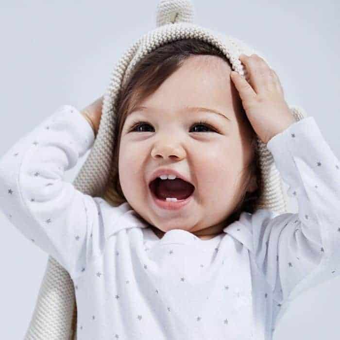 smiling baby wearing white organic baby clothes with bear sweater