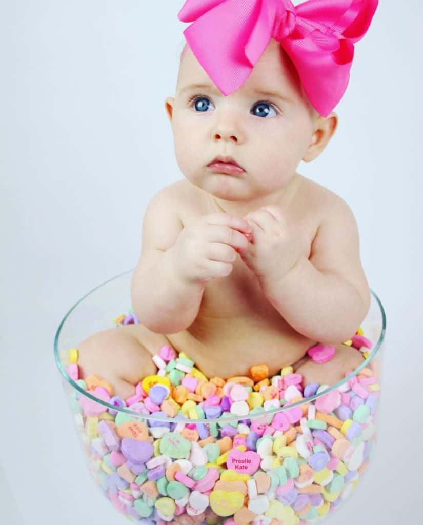 Baby sitting in bowl of Sweat Hearts with large pink bow on head