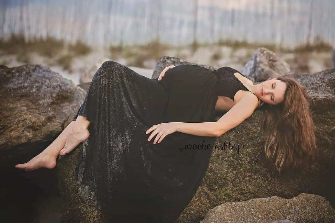 maternity session with pregnant woman in black dress lying on rocks