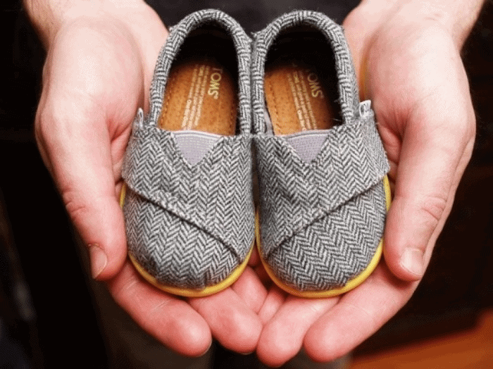 hands holding a pair of baby sized Toms shoes