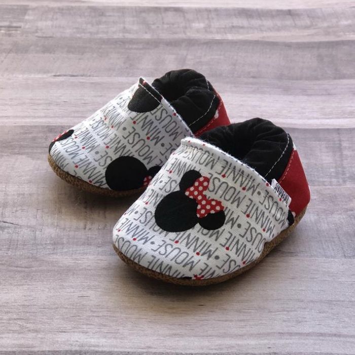 Tiny cloth moccasins made from fabric that says "Minnie Mouse" with small Minnie Mouse head.