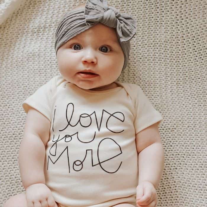 Baby with bow wearing an 'I love you more' onesie
