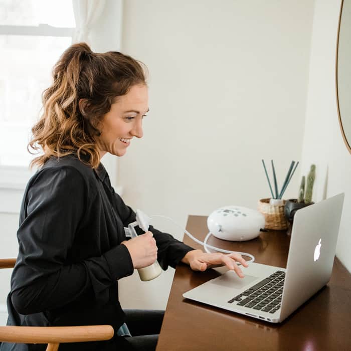 woman pumping breast milk with a breast pump while sitting in front of laptop