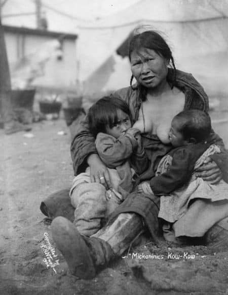 Black and white old photograph of Indigenous woman tandem nursing children outdoors in Alaska