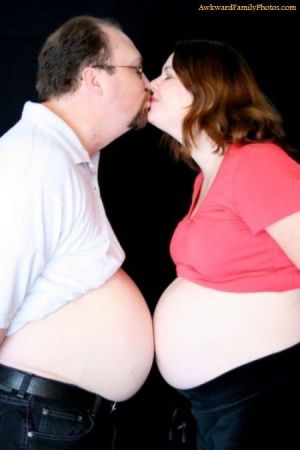 Couple stands and kisses while bare bumps touch.