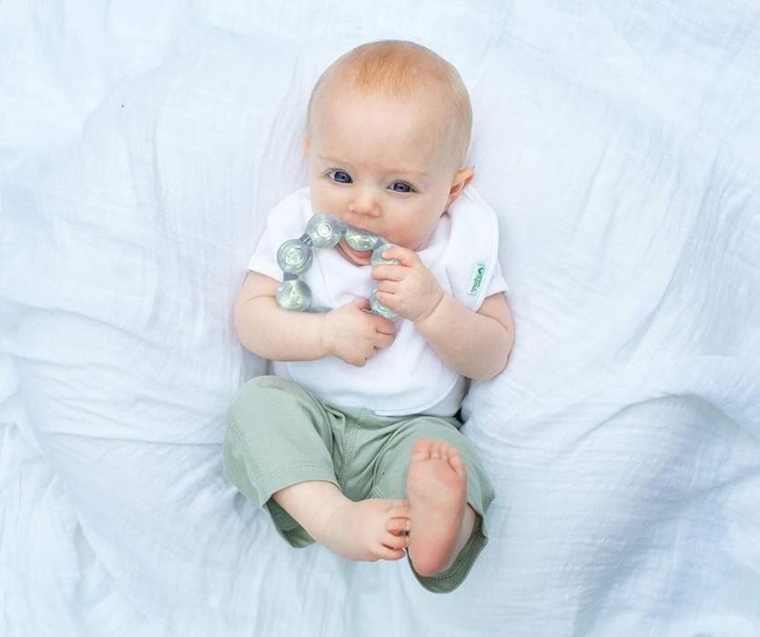 Overhead shot of baby wearing white and green laying on their back chewing on Green Sprouts Cool Ring teether