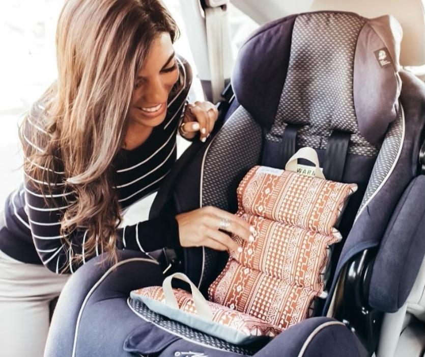 Interior of car showing car seat with Little Bum Cooler being placed by smiling woman.