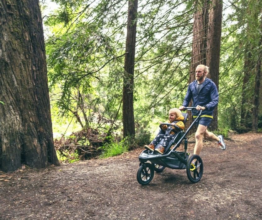 Photo of man jogging through forest pushing toddler in Veer Switch&Roll jogging stroller.