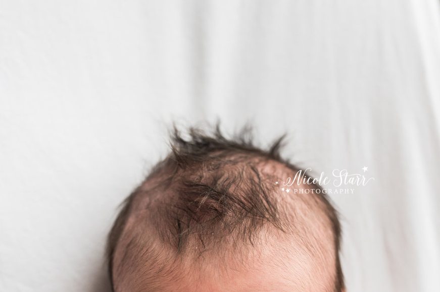 Close up color photo of the very top of newborn's head of hair against a white sheet. 