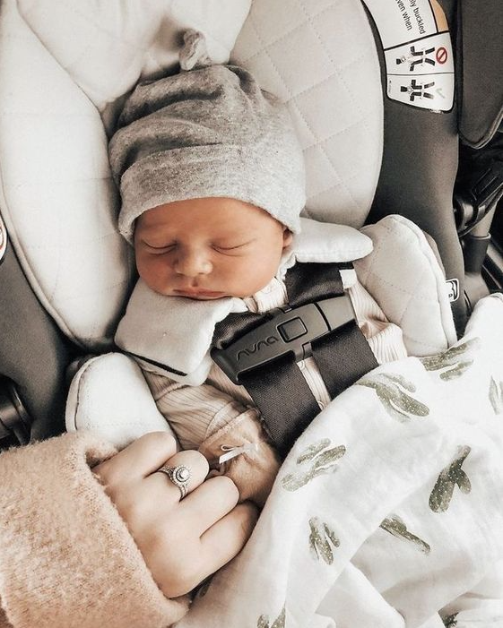 Color photo of newborn strapped into carseat with mom's hand holding on.