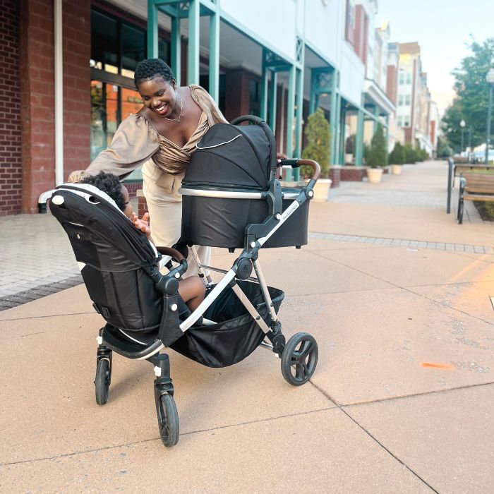 Woman on the sidewalk with Mockingbird single to double stroller with toddler in seat and bassinet attached.