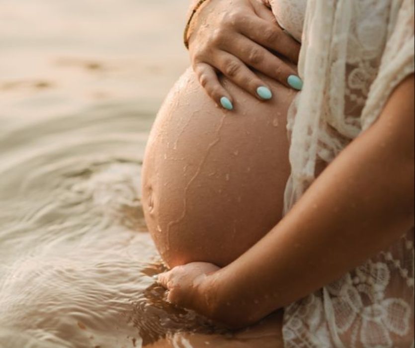 close up image of woman holding her baby bump in water