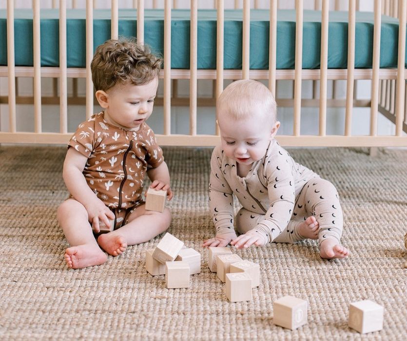 two babies playing with blocks in front of a crib