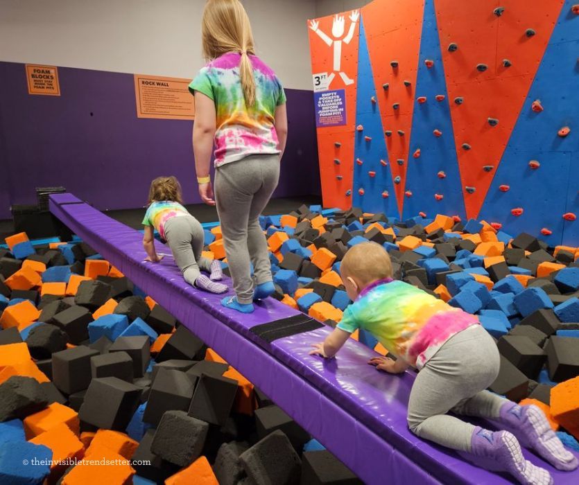 Three kids going across a purple balance beam in tie-dye shirts.