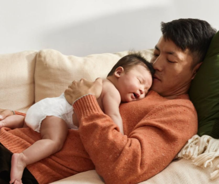 dad on the couch holding baby wearing coterie diapers