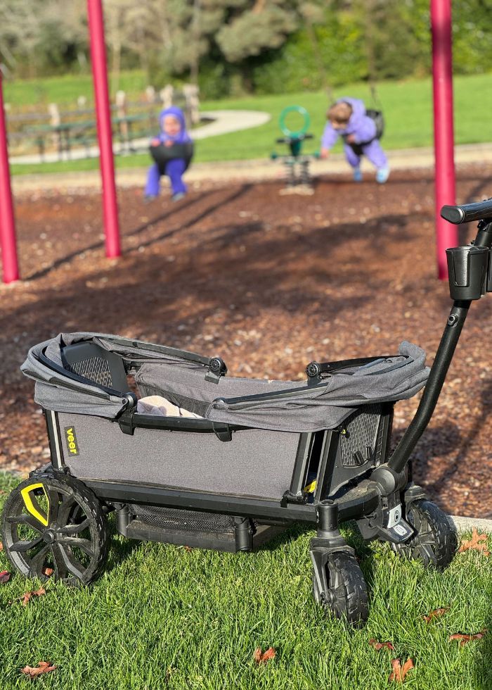 all terian veer wagon at the park with two toddlers on the swings in the background